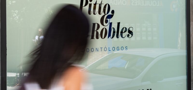 Mujer pasando por el escaparate de Pitto & Robles Odontólogos